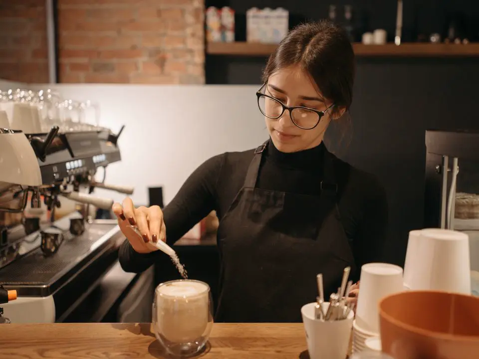 Barista sipa šećer iz kesice u kafu na šanku kafića